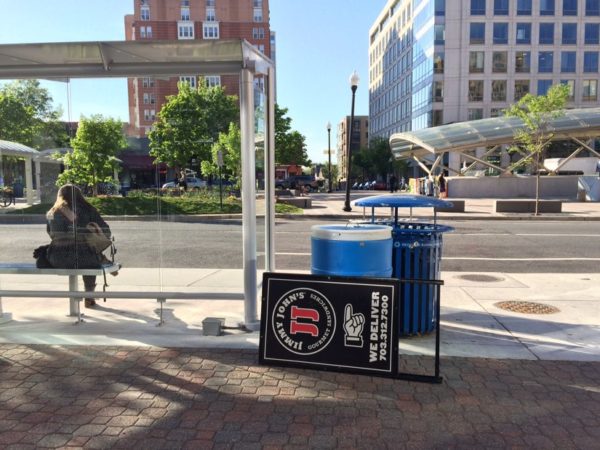 Street scene in Clarendon on 4/20/16. Woman sitting at bus stop with Clarendon Metro in background.